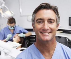 Portrait,Of,Dental,Nurse,With,Dentist,Examining,Patient,In,Background