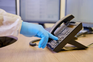 A doctor in medical uniform dials a number on a black phone